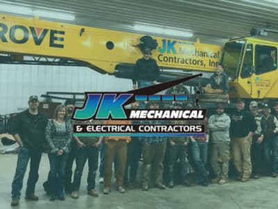 Men and women standing in front of a crane with JK Mechanical & Electrical Contractors logo
