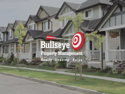 Row of small homes in a neighborhood with green grass and potted plants on the porches with Bullseye Property Management logo