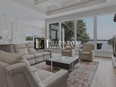 Living room with upscale furniture, fireplace overlooking modern kitchen with lake view windows with Fieldstone Family Homes logo