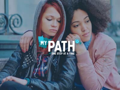 Two disadvantaged teens looking pensive while one comforts the other with MyPath logo