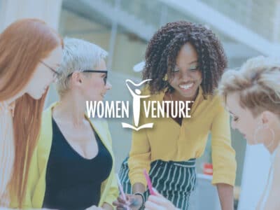Four happy women discussing books and documents with WomenVenture logo