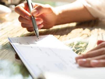 Businesswoman's Hand Signing Cheque On Wooden Desk