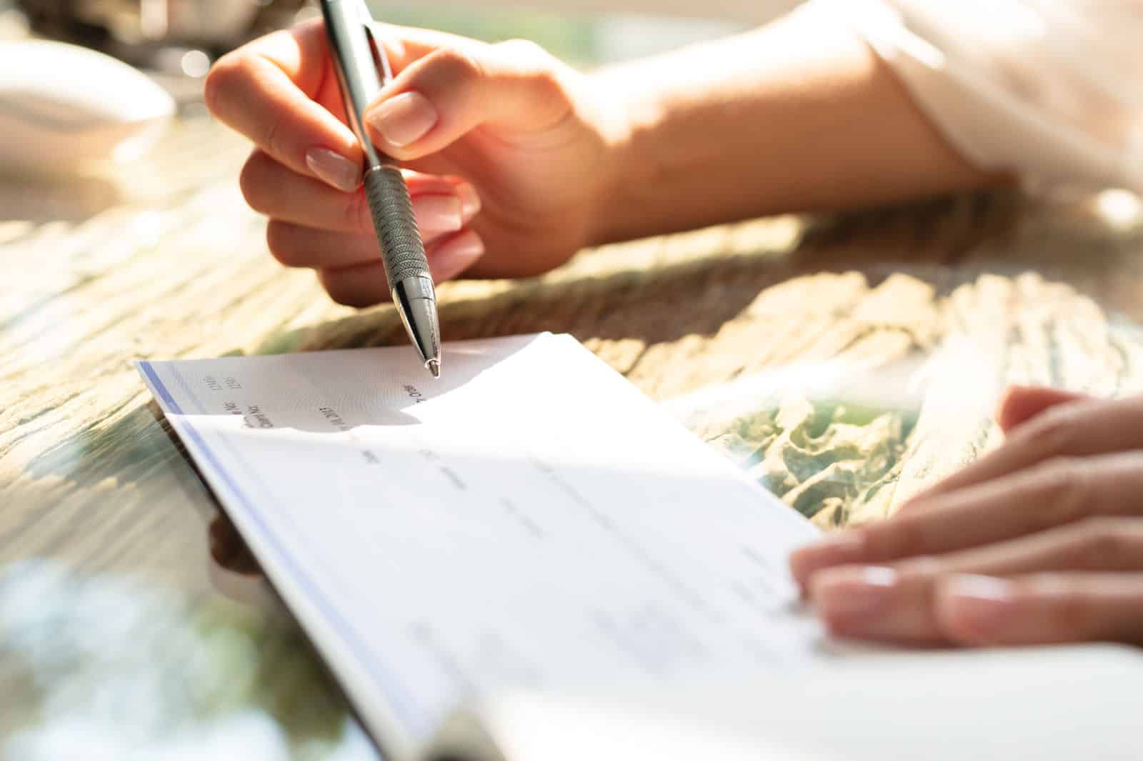 Businesswoman's Hand Signing Cheque On Wooden Desk