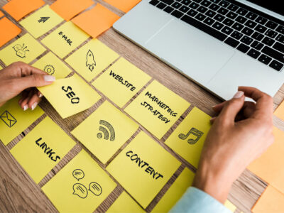 Woman touching sticky note with seo lettering near laptop on desk