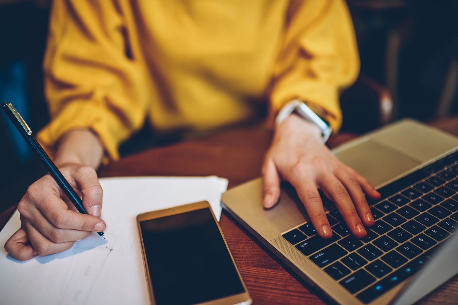 Female hands with pen writing notes next to laptop computer