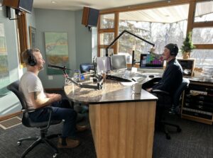 Two men in a radio station studio talking into microphones