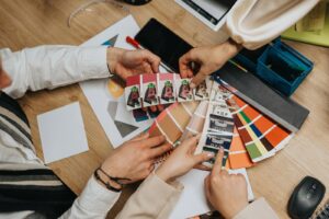 A group of designers and colleagues compares color swatches and samples on a wooden desk